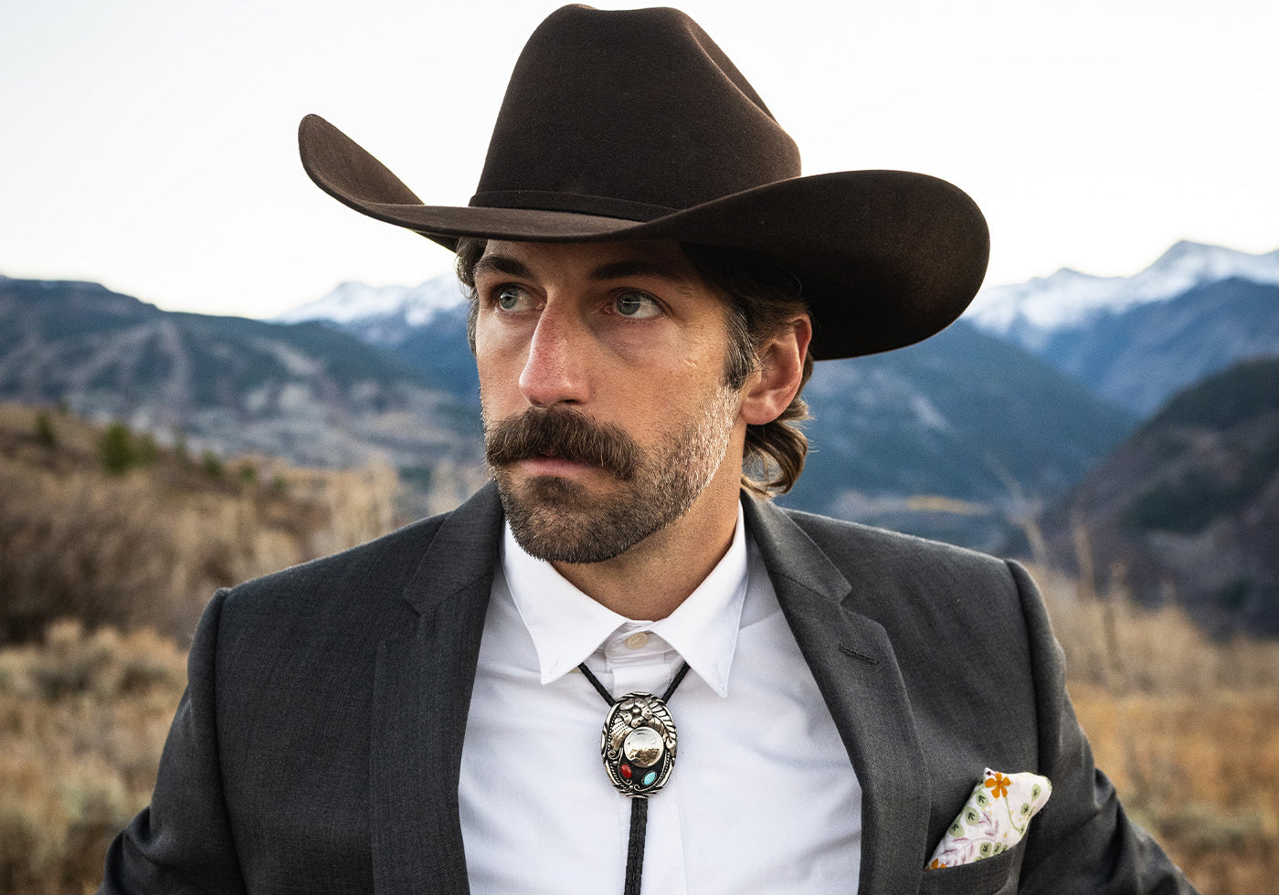 Man wearing a cowboy hat and suit with a mountainous background