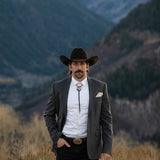 Man in a suit and cowboy hat standing in a mountainous landscape