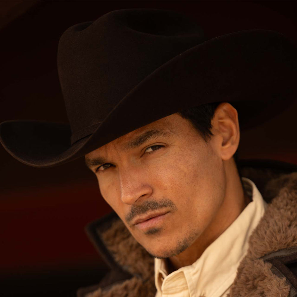 Man wearing a 6X Real brown cowboy hat, jacket with brown fur lining on the inside edges, and off-white shirt