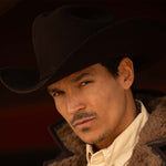 Man wearing a 6X Real brown cowboy hat, jacket with brown fur lining on the inside edges, and off-white shirt