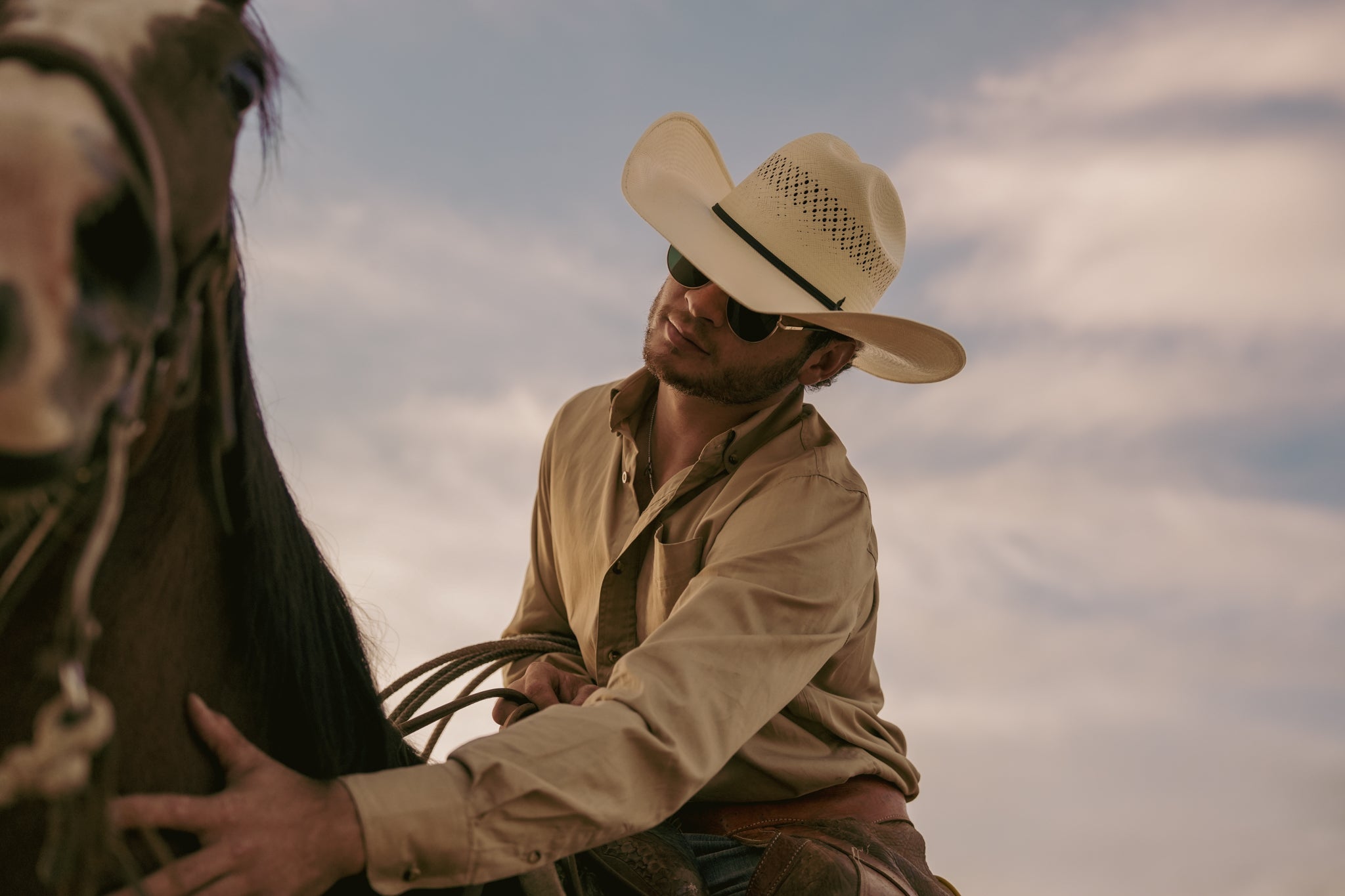 Man in cowboy hat sitting on a horse against a cloudy sky