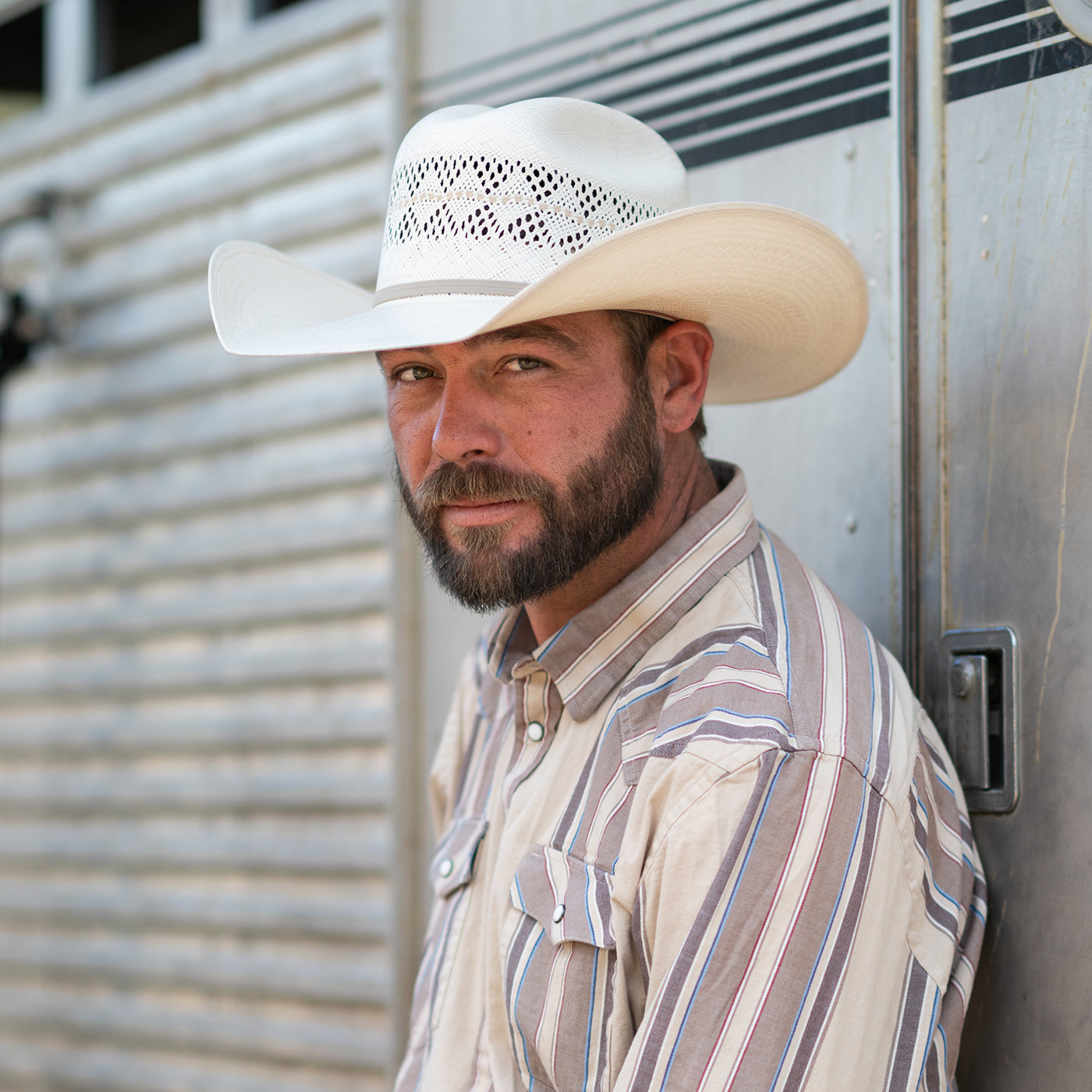 A white cowboy hat with a black band and white woven pattern band, resting on natural rocks outdoors